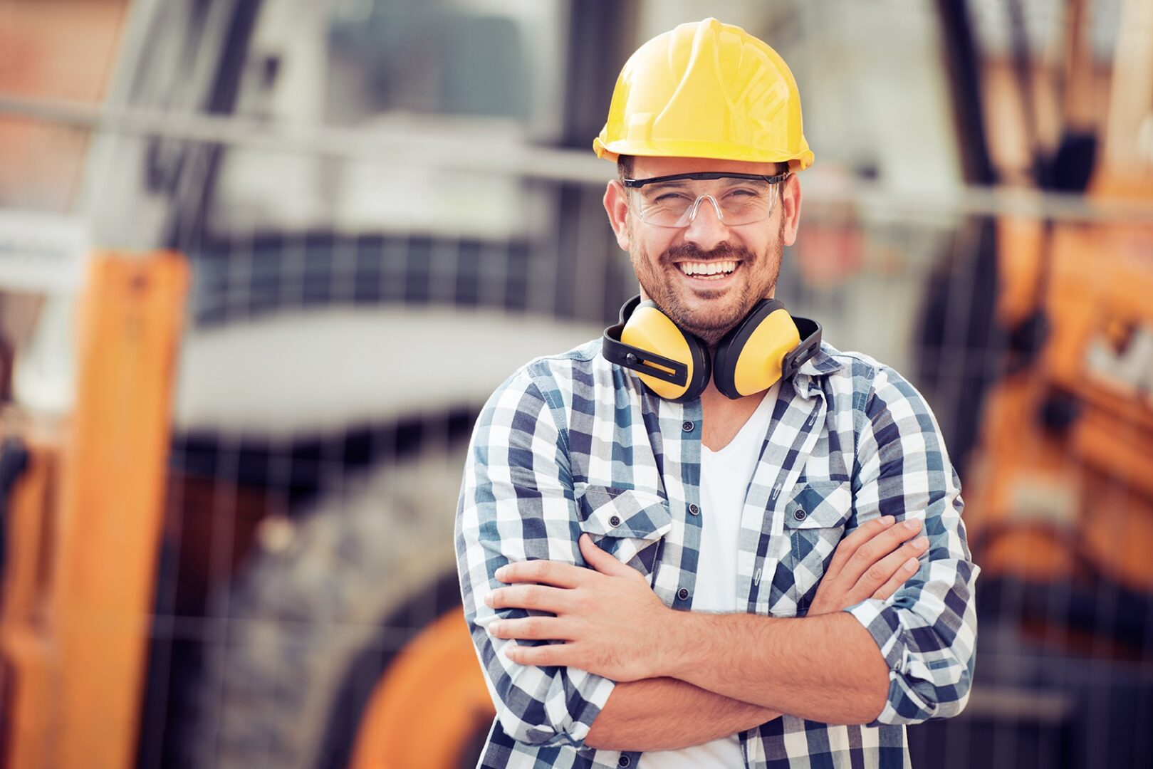 A smiling construction worker stands in front of an excavating machine.